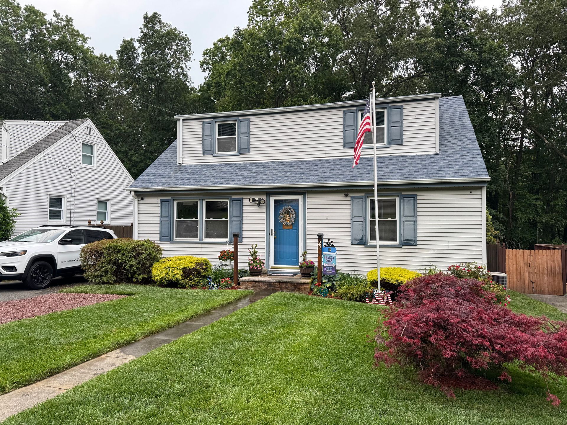 A two-story house with white siding, blue shutters, and a blue front door, with a manicured lawn and a small red tree.