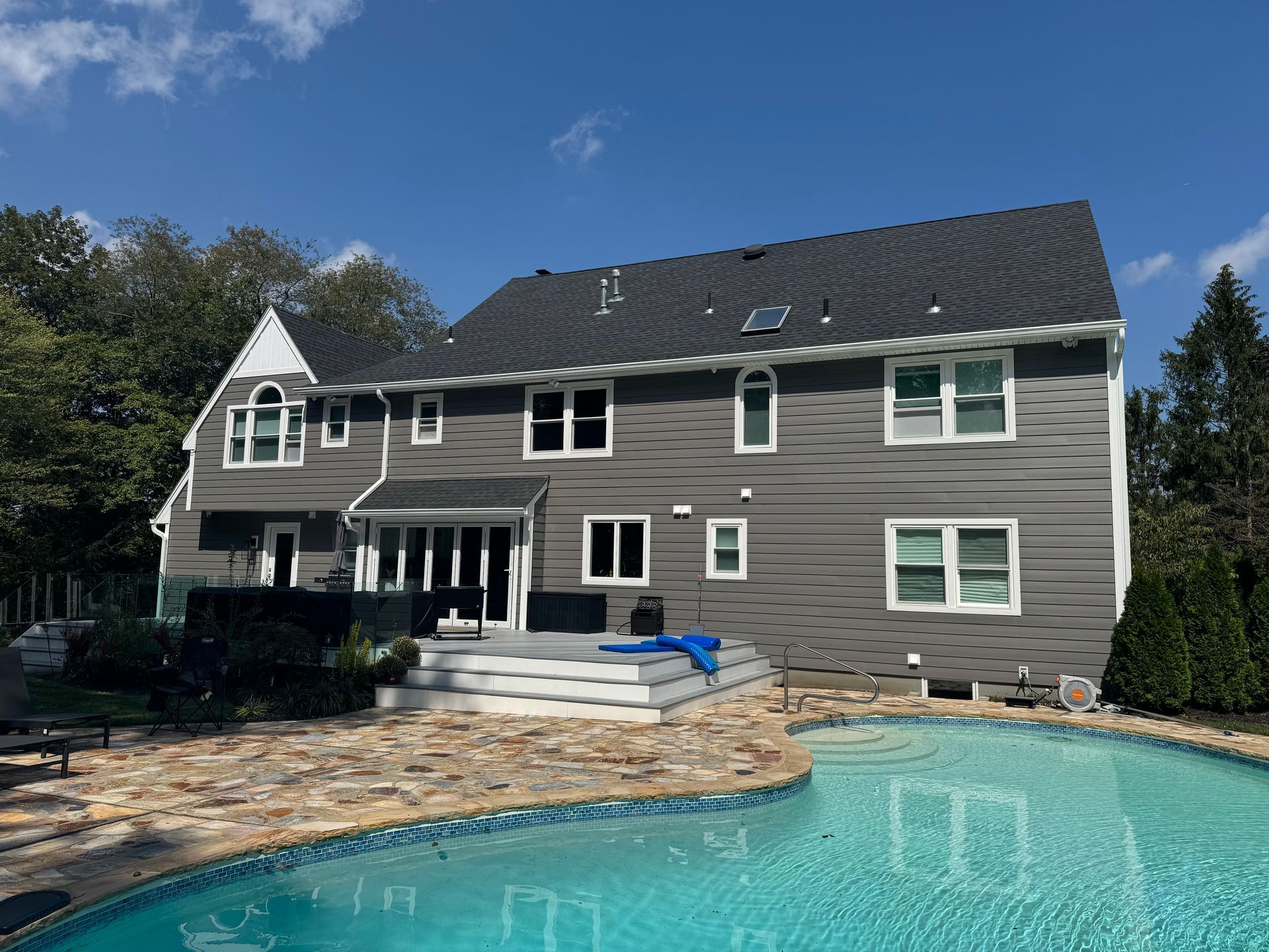 A multi-story gray home with a swimming pool and patio in the backyard under a blue sky.