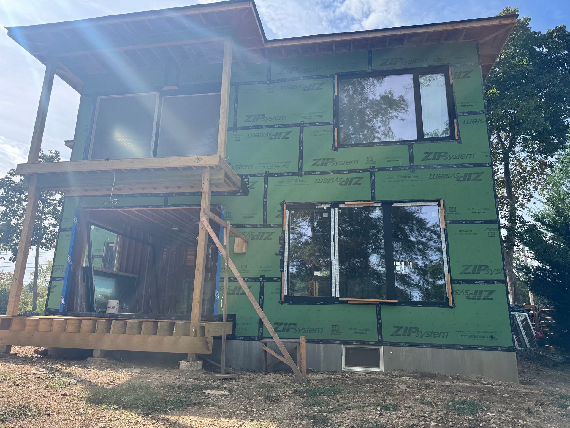A two-story house under construction, covered in green ZIP System sheathing with installed windows and an open porch.