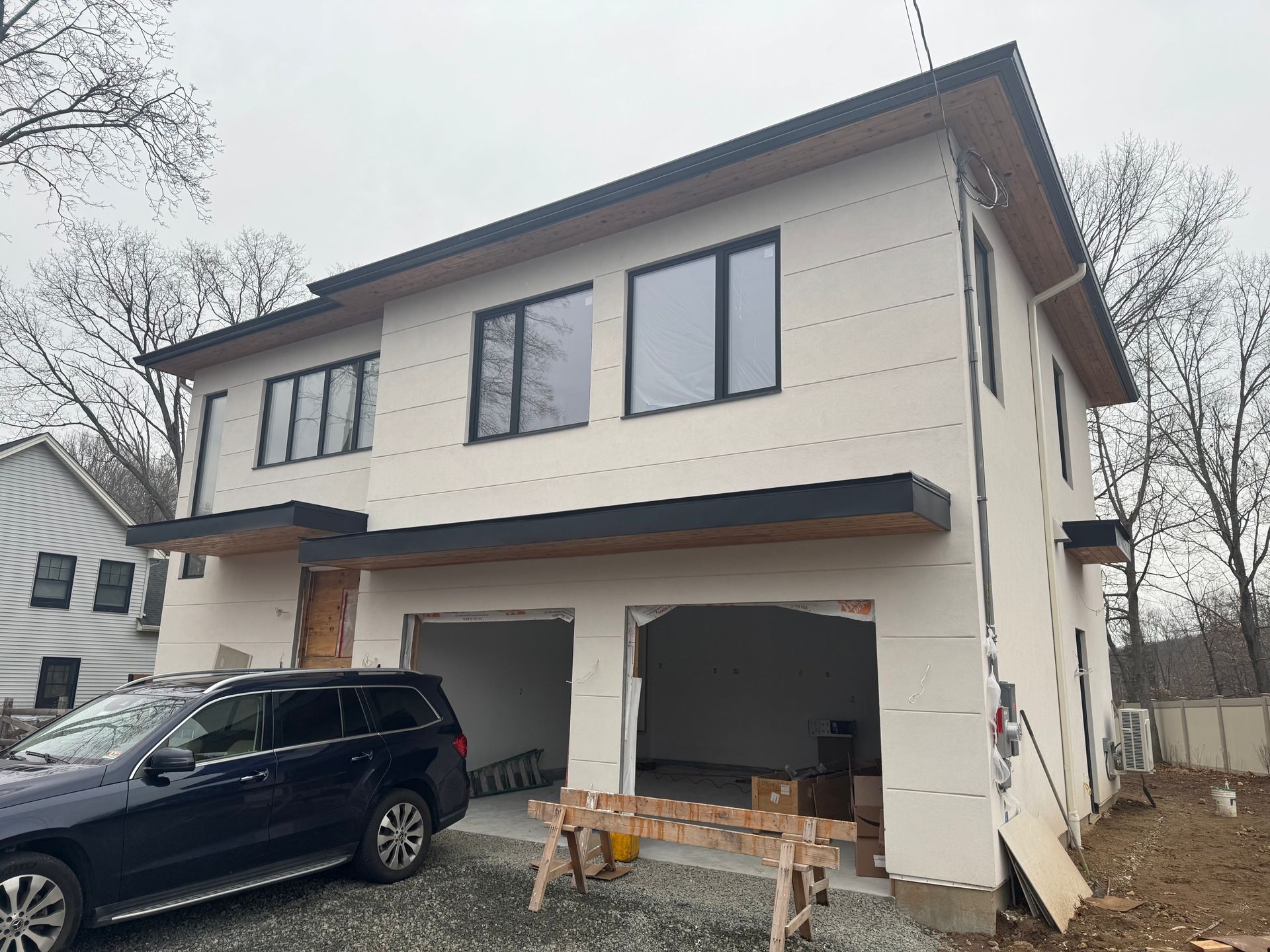 A two-story house under construction with a dark blue SUV parked in front of the open garage bays.