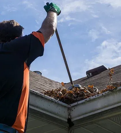 Technician cleaning leaves from home gutters during fall maintenance in Central Iowa