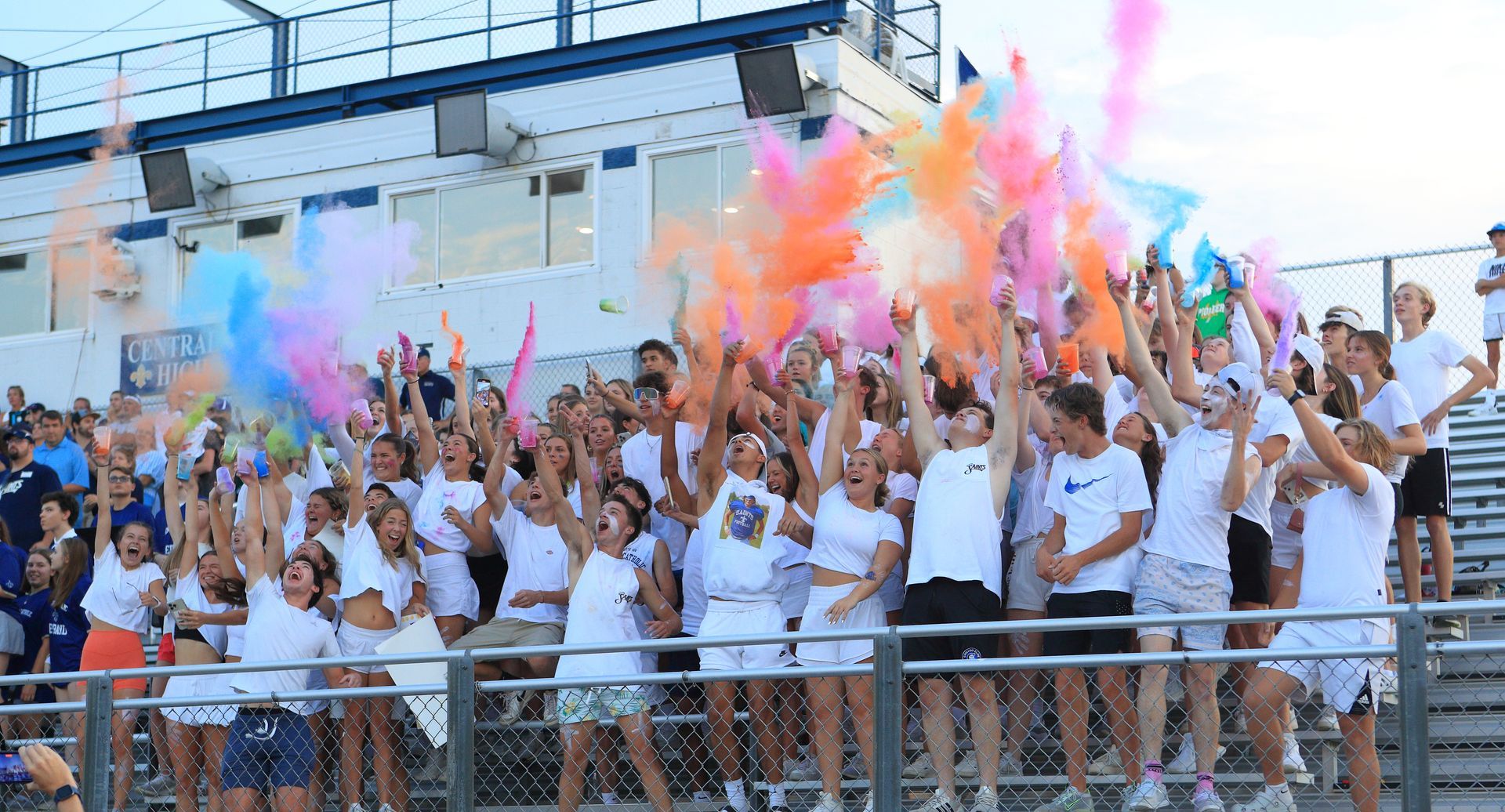 A large group of people are standing in a stadium holding colorful confetti.
