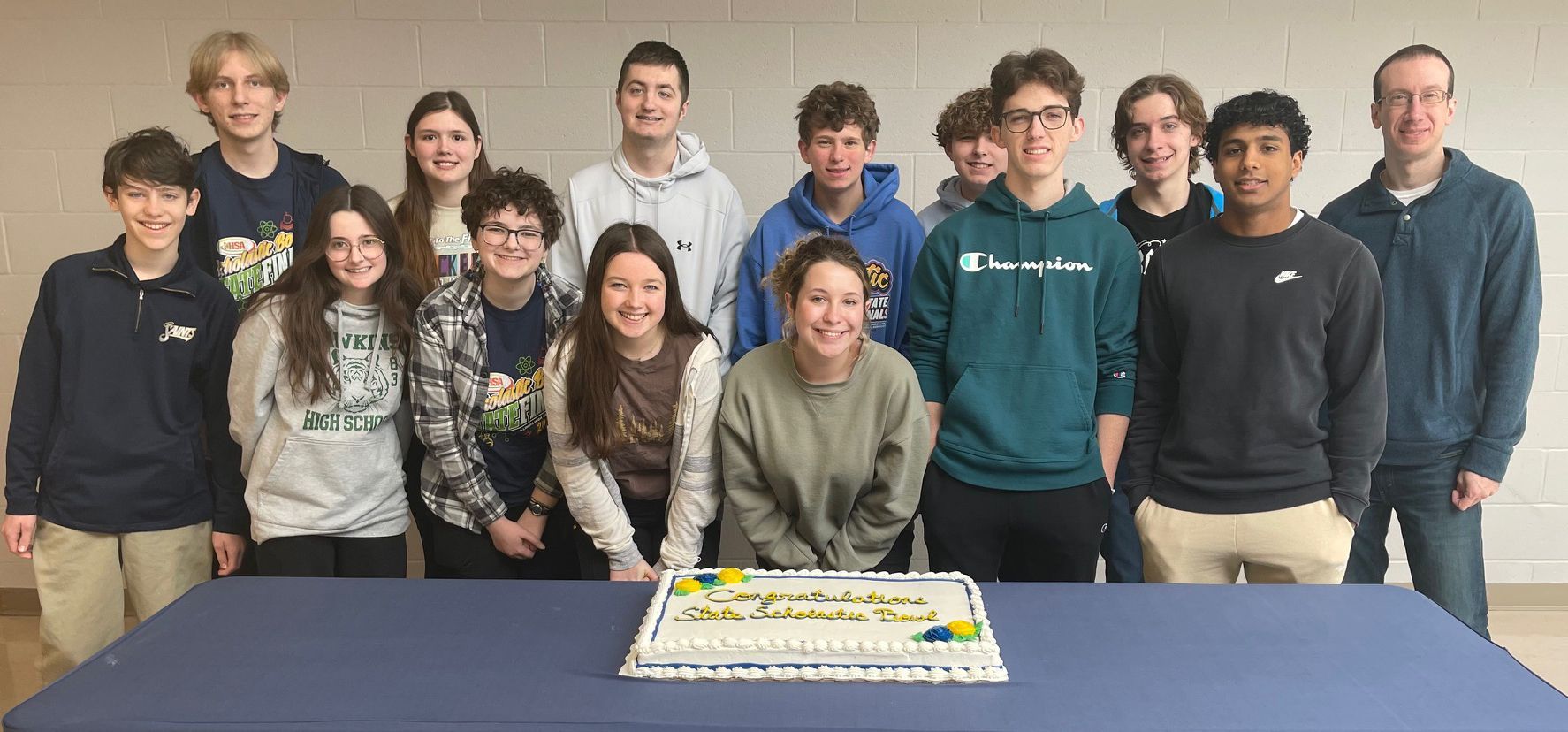 A group of young people are posing for a picture in front of a cake.
