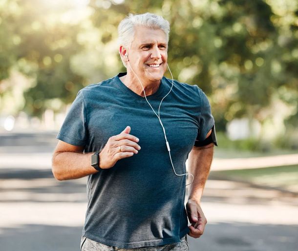 An older man is running in a park with headphones on.