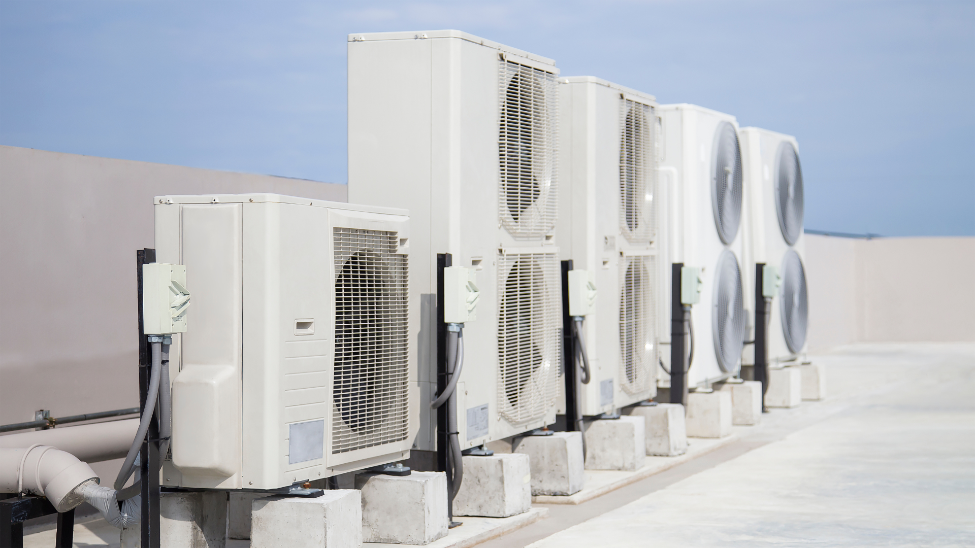 A row of air conditioners are lined up on the roof of a building.