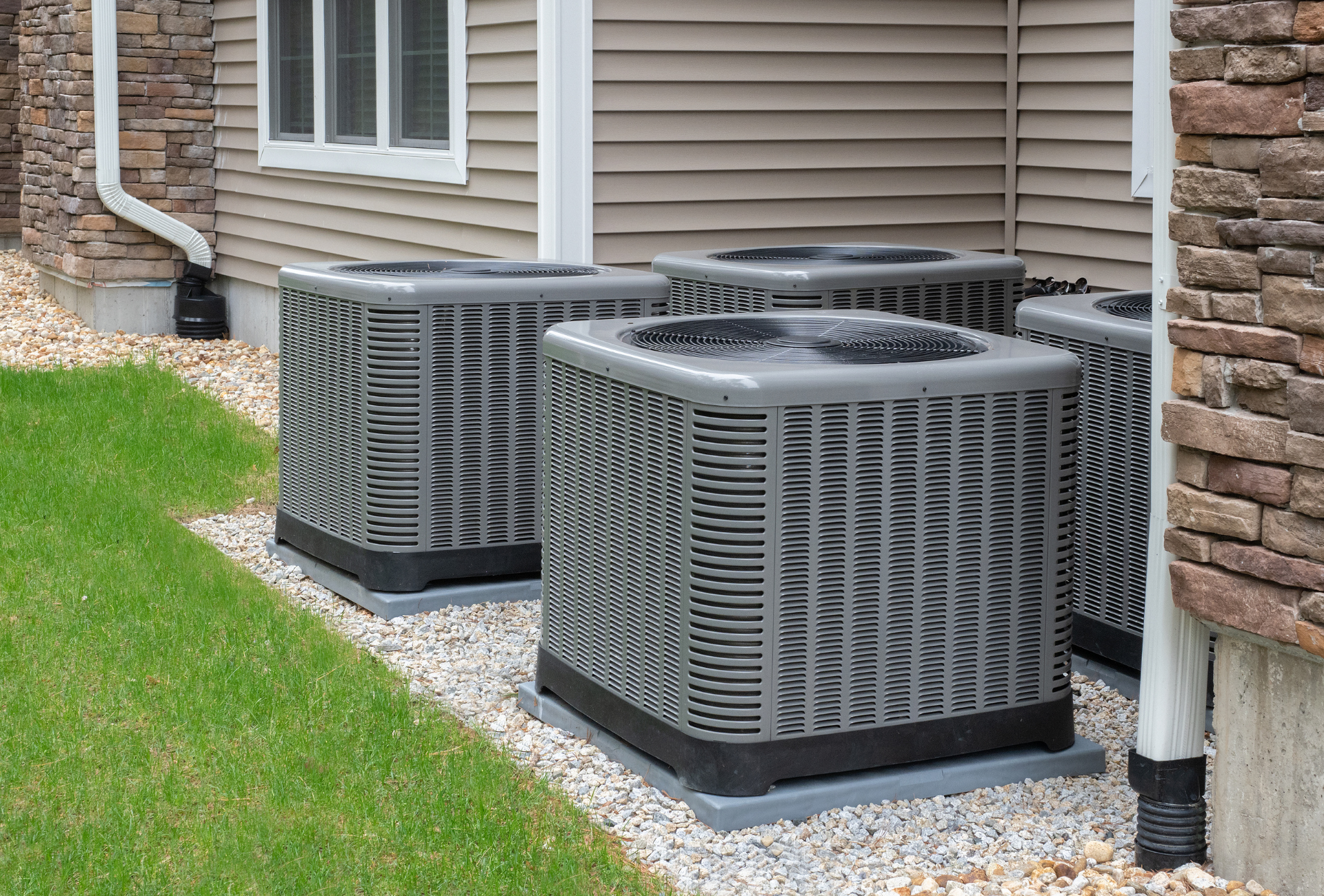 Three air conditioners are sitting on the side of a house.