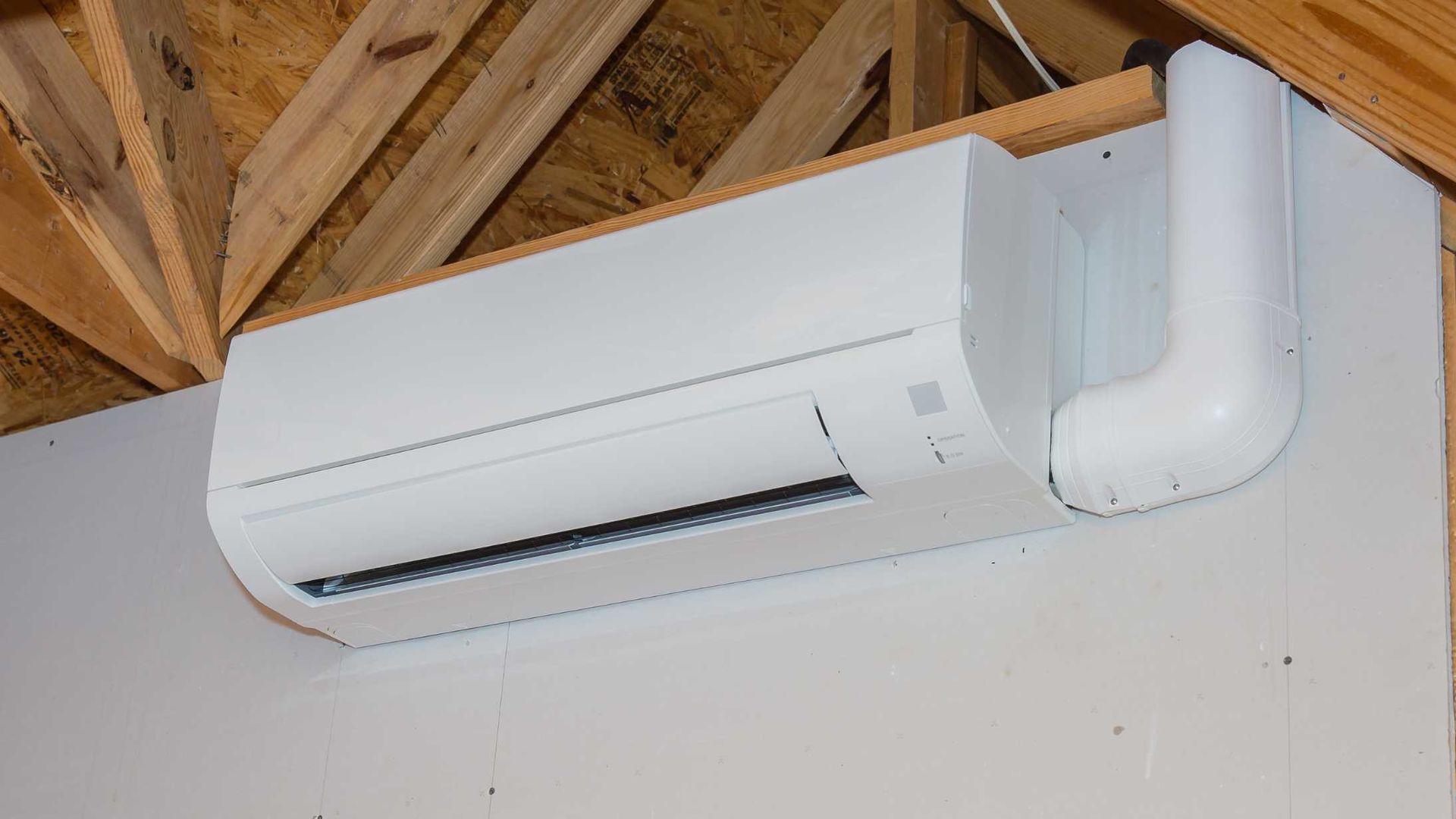 A white air conditioner is hanging from the ceiling of a room under construction.