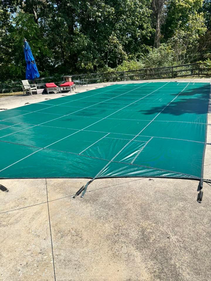 A green swimming pool cover is sitting on top of a concrete patio.