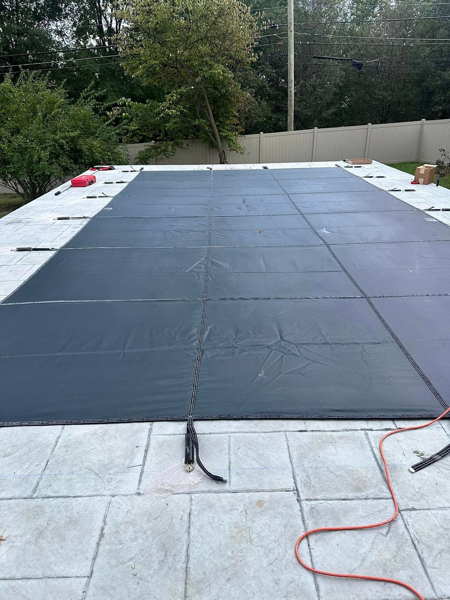 A large black tarp is covering a large swimming pool.