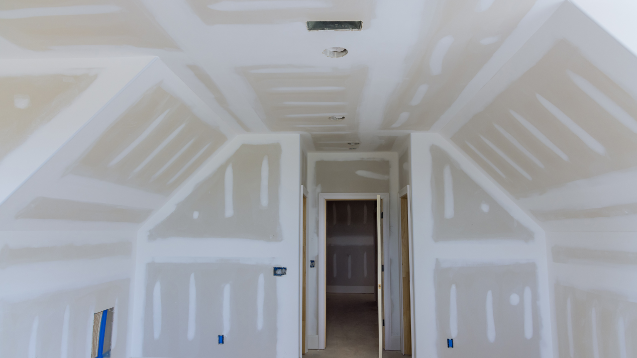 Unfinished room interior with drywall walls and ceiling, hallway leading to door.
