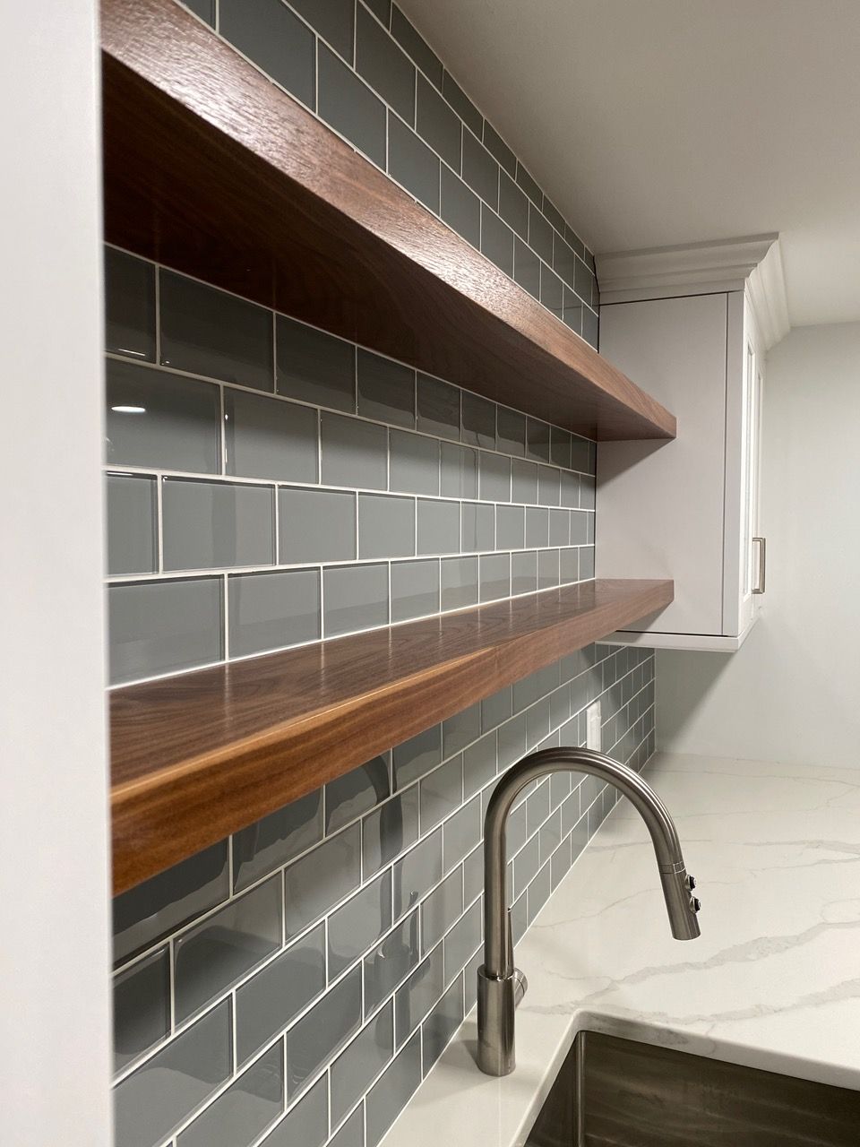 Gray tiled backsplash with floating wood shelves above a sink and faucet.