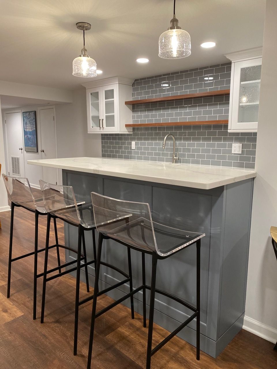 Bar area with gray cabinets, quartz countertop, glass stools, and pendant lights.