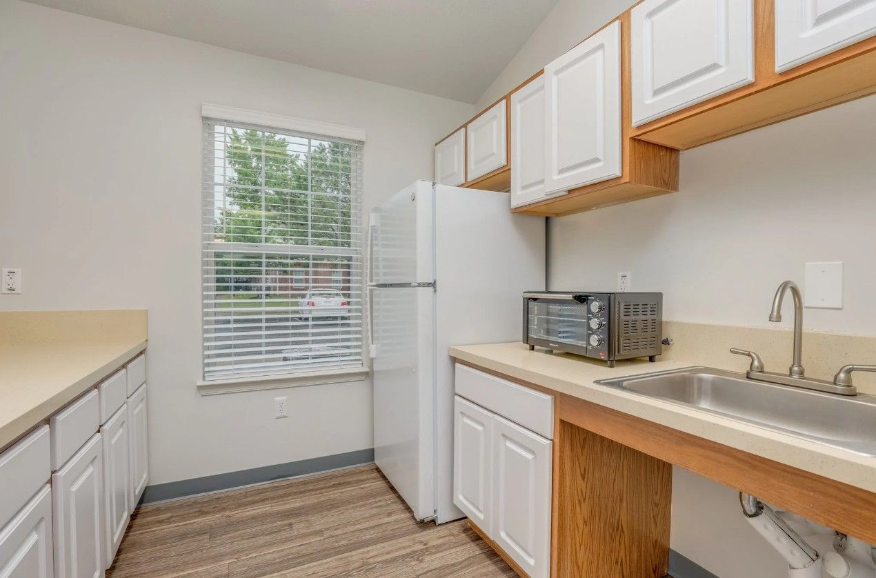 A kitchen with white cabinets, light-colored countertops, a white refrigerator, a toaster oven, and a sink by a window.