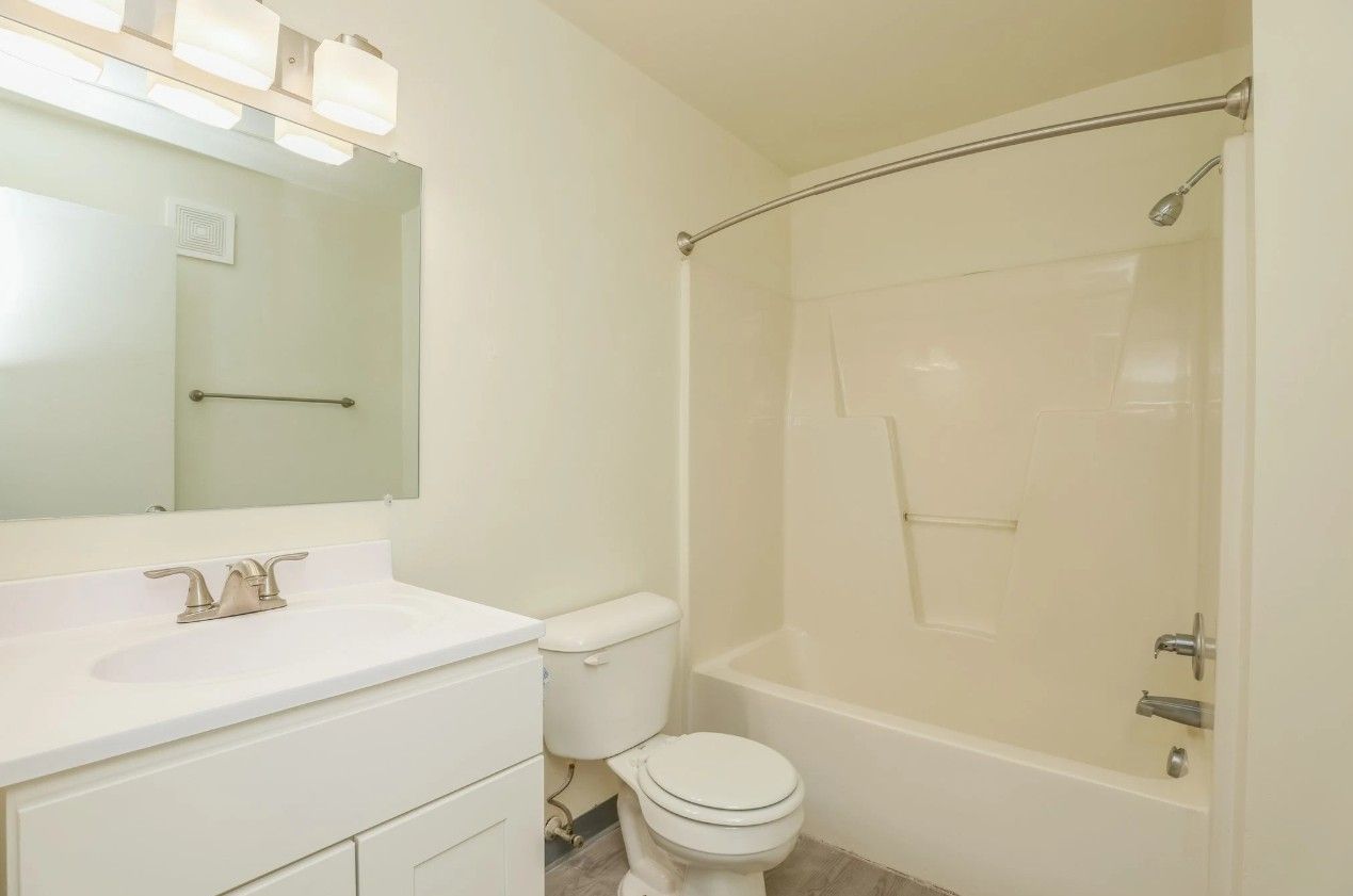 A white bathroom featuring a vanity with a sink, a toilet, and a combination bathtub and shower with a curtain rod.
