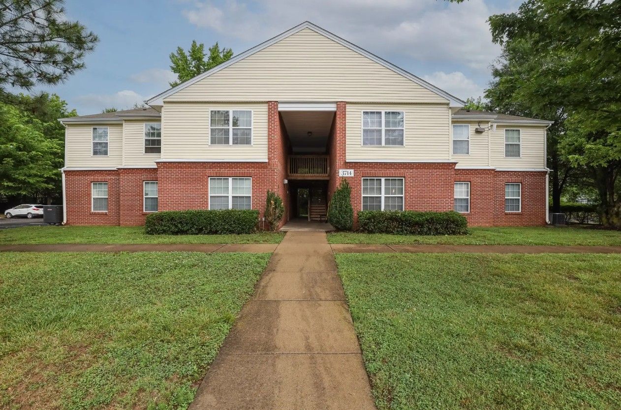 A two-story apartment building with a brick ground floor, cream siding upper level, and a central entrance walkway.