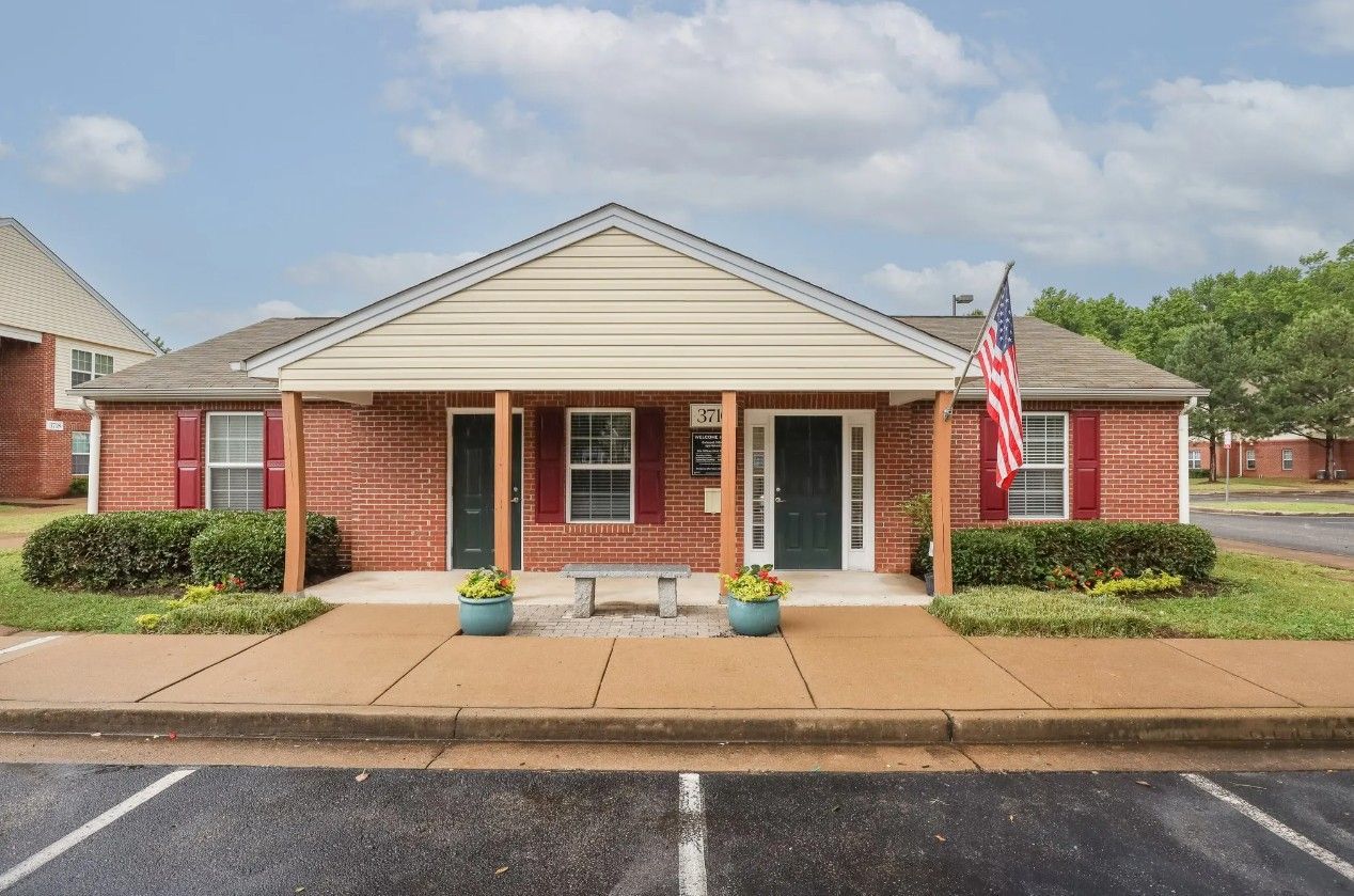 A one-story brick office building with red shutters, a cream-colored gabled roof, and a small bench at the entrance.