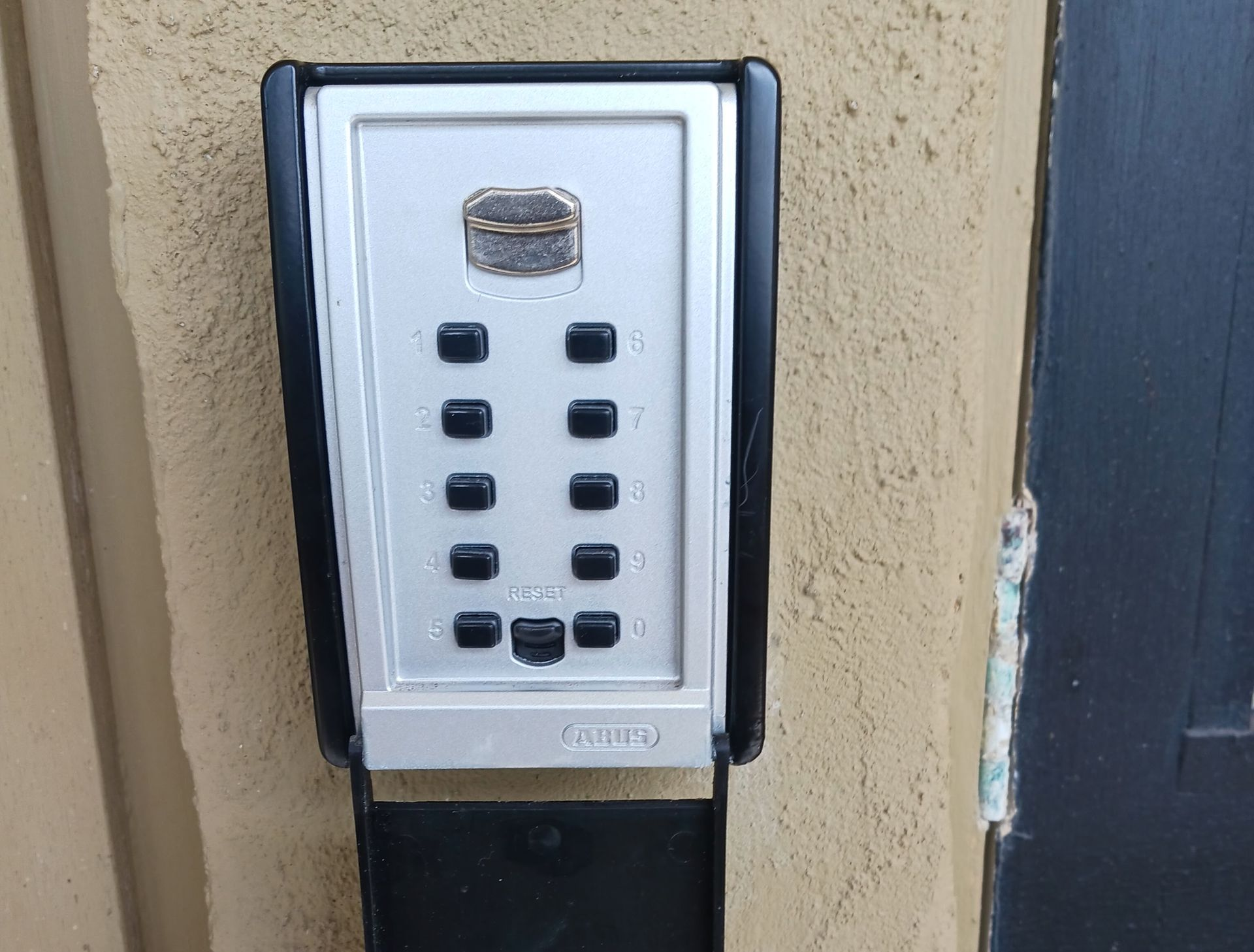 Key safe with keypad mounted on a stucco wall next to a dark window. The door is open— Yamba Locksmiths in Yamba, NSW
