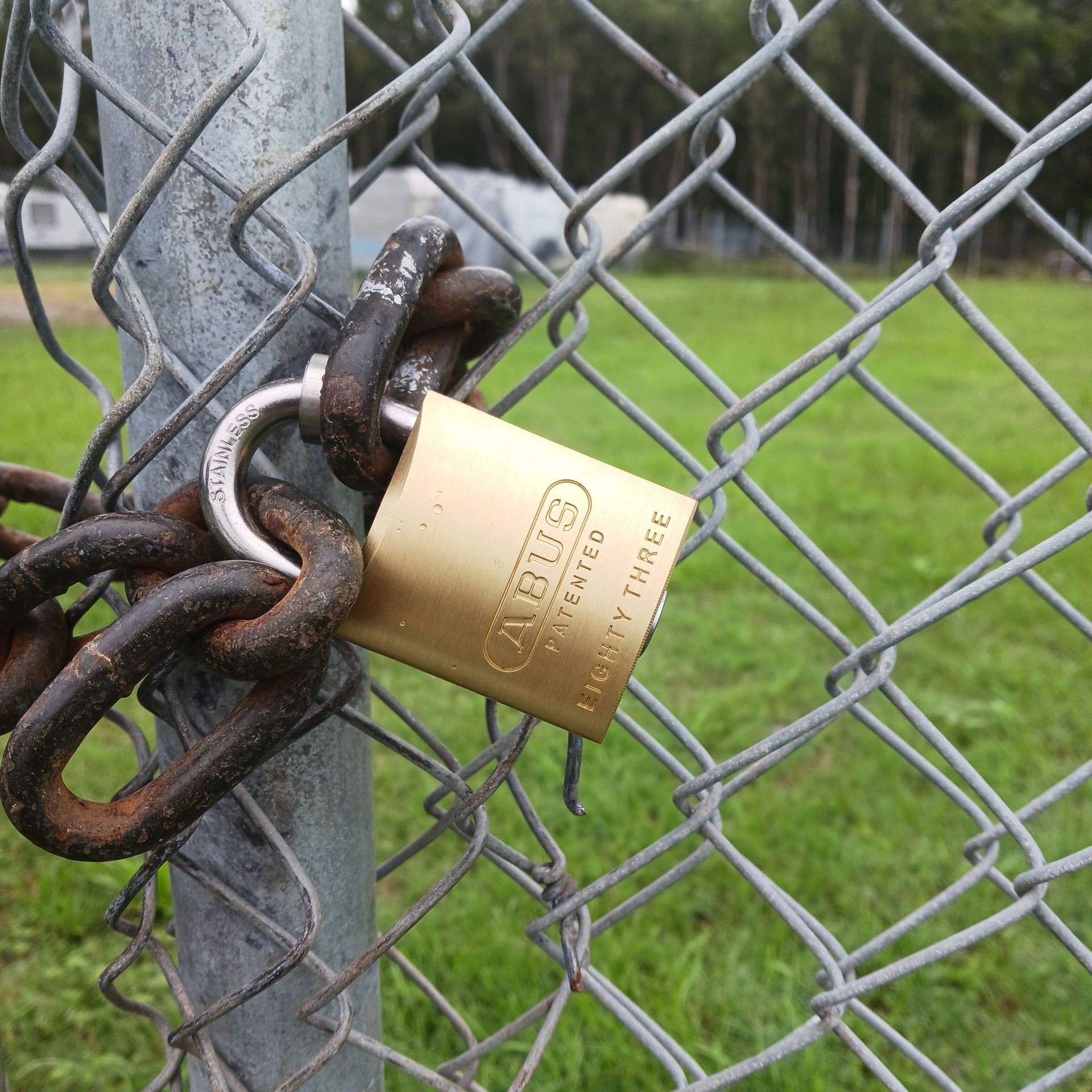 Gold padlock securing a rusty chain on a chain-link fence, grassy field in background— Yamba Locksmiths in Yamba, NSW