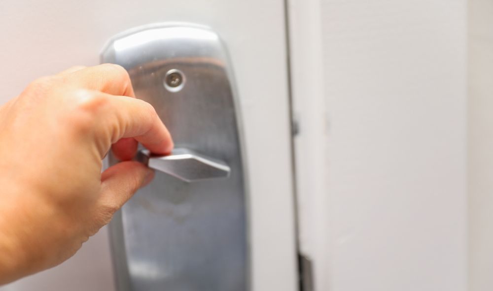 Hand Turning a Lever Handle on a Silver Door Lock, Opening a White Door — Yamba Locksmiths in Yamba, NSW