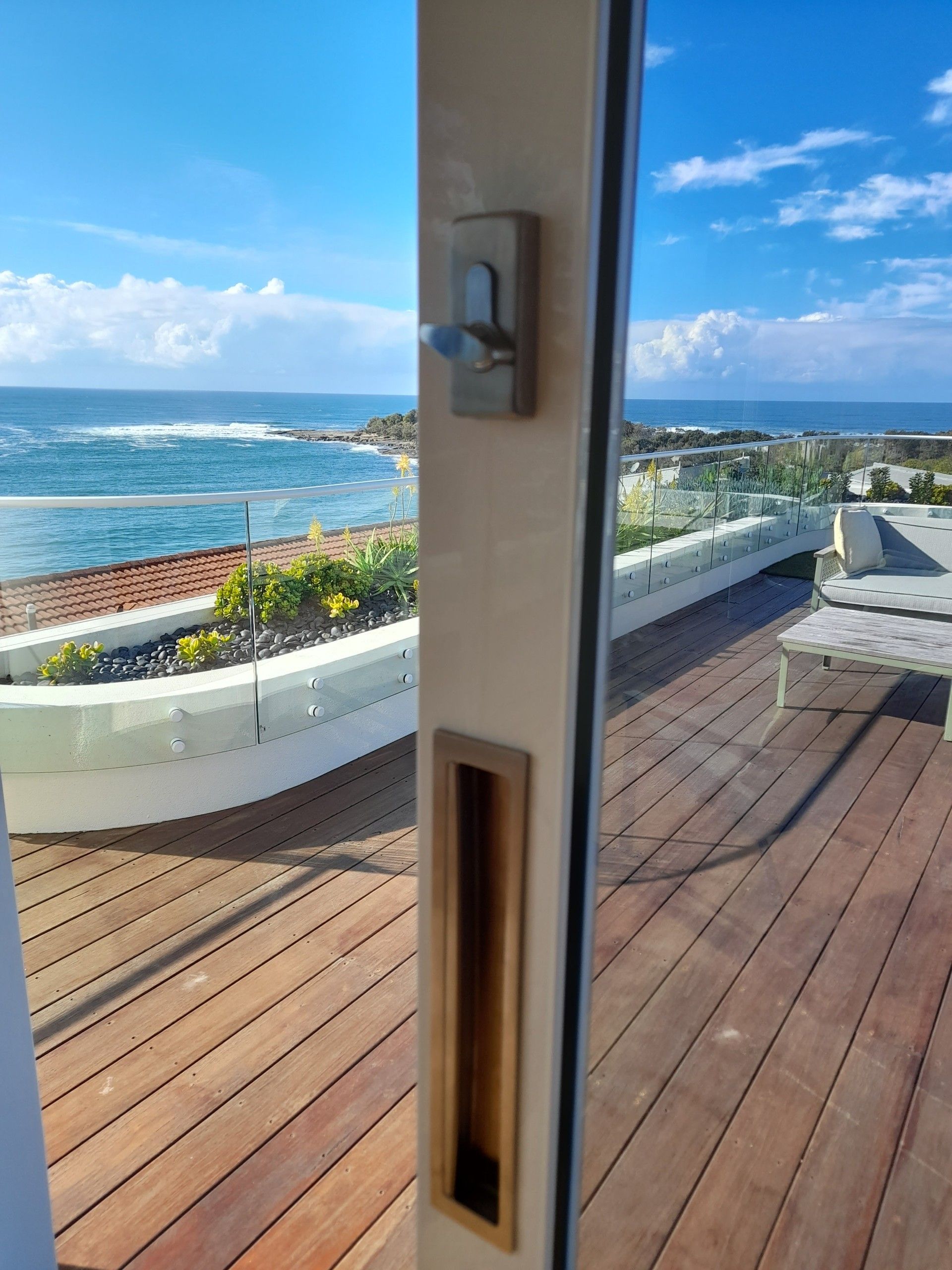View through open sliding glass door to ocean and deck. Door hardware visible— Yamba Locksmiths in Yamba, NSW