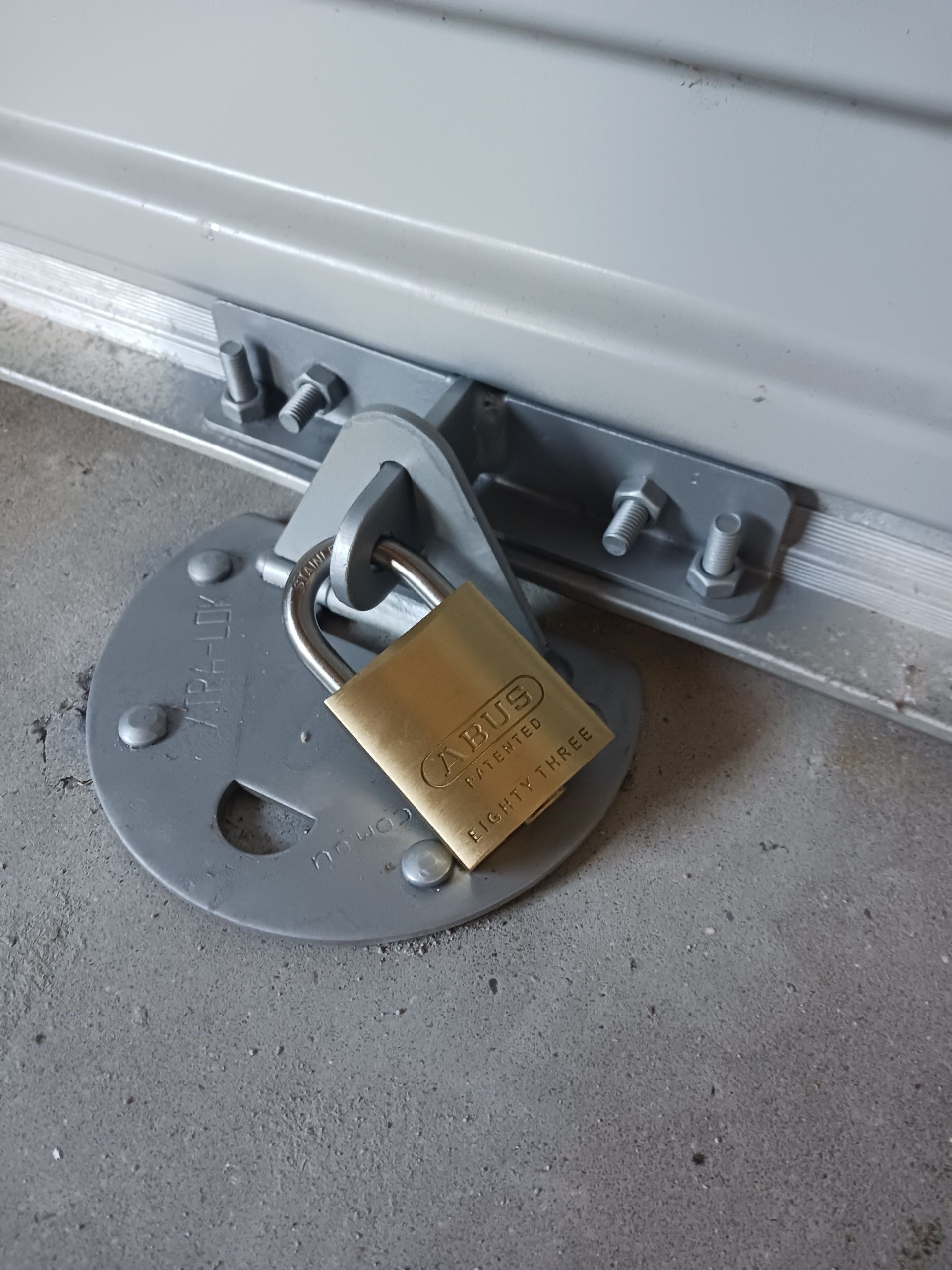 Gold padlock securing a gray metal garage door with a bolt plate on a concrete floor— Yamba Locksmiths in Yamba, NSW