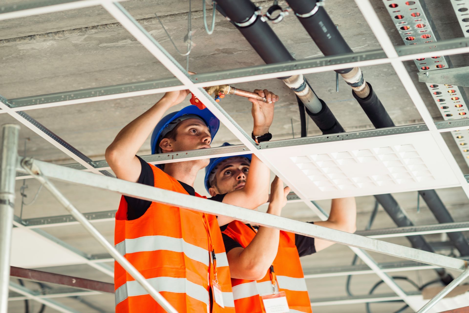 Two construction workers are working on the ceiling of a building.