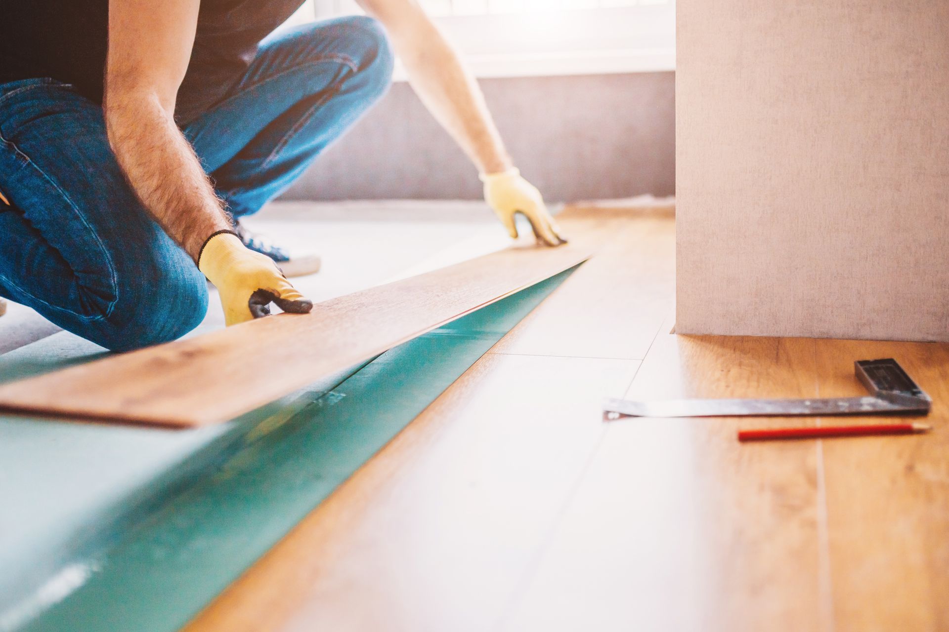 A man is kneeling down to install a wooden floor.