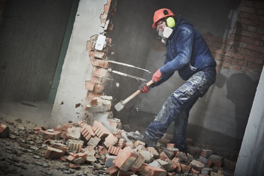 A man is breaking a brick wall with a hammer.