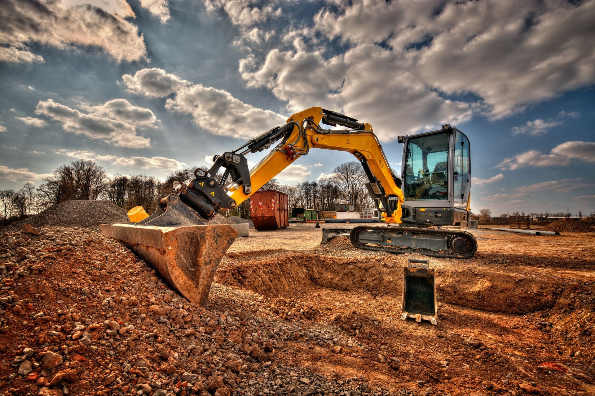 A yellow excavator is digging a hole in a dirt field.