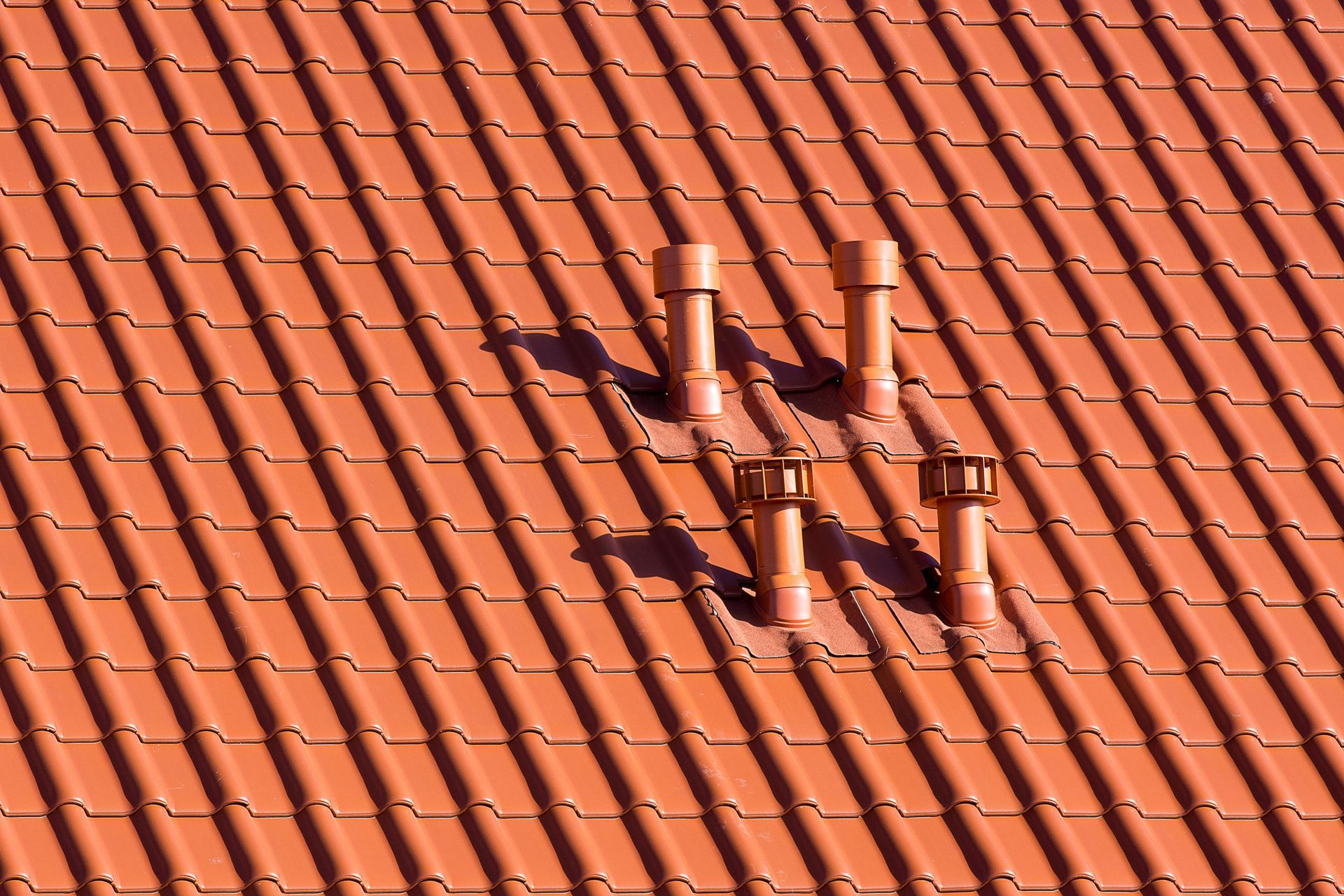 Red tiled roof with four vent pipes casting shadows.