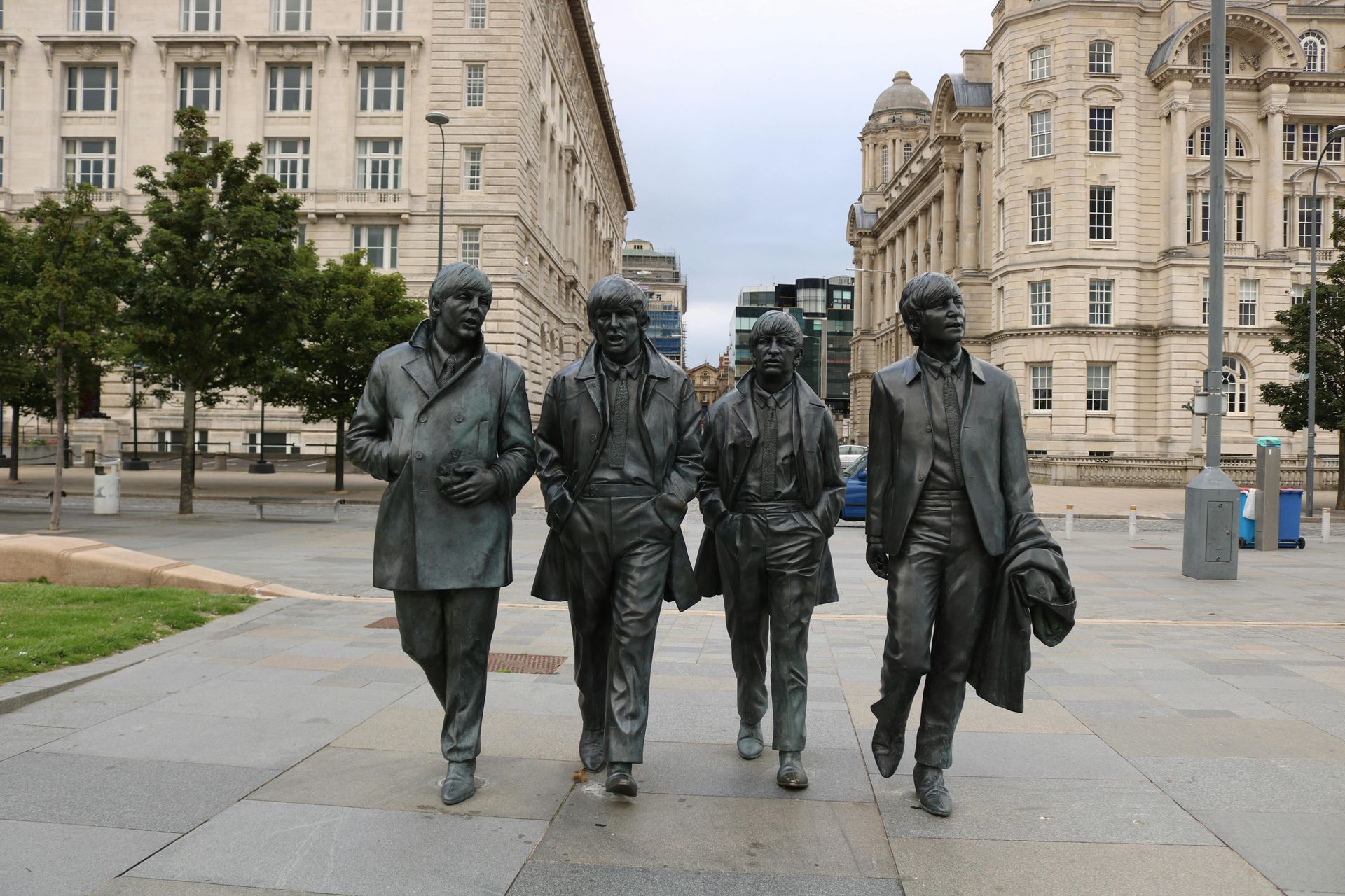 Bronze statue of The Beatles walking on a Liverpool city street. Buildings in background.