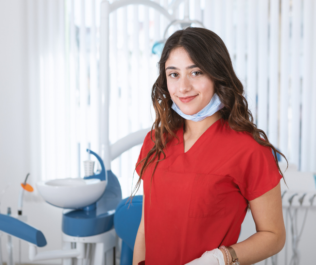 Woman in red scrubs standing in a dental clinic with a mask under her chin