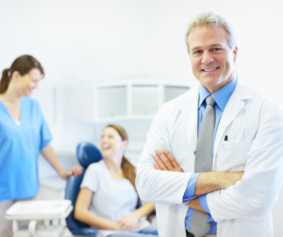 Smiling doctor in white coat stands in clinic with two blurred staff members in the background