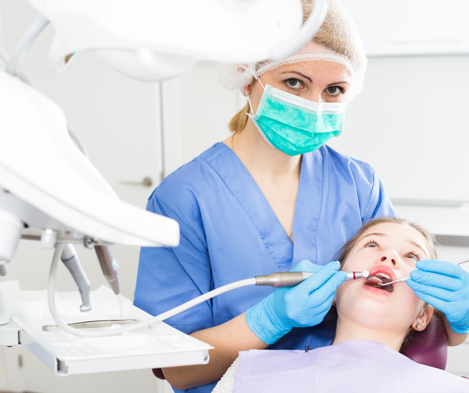 Dentist in blue scrubs and mask treating a patient in a bright dental clinic