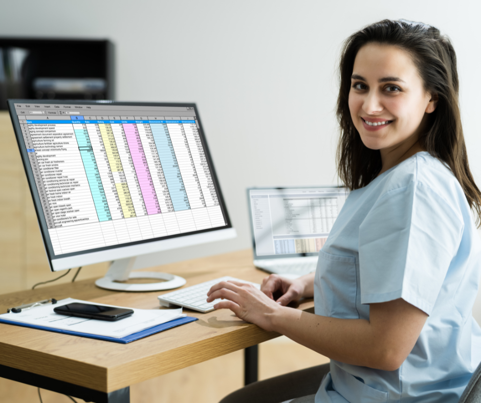 Smiling woman at a desk using a desktop computer with a spreadsheet on screen