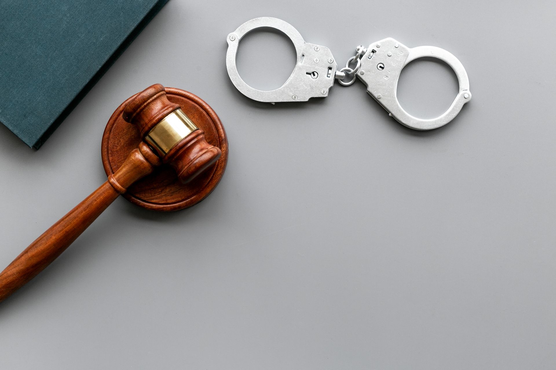 Wooden gavel and handcuffs on gray surface beside a book.