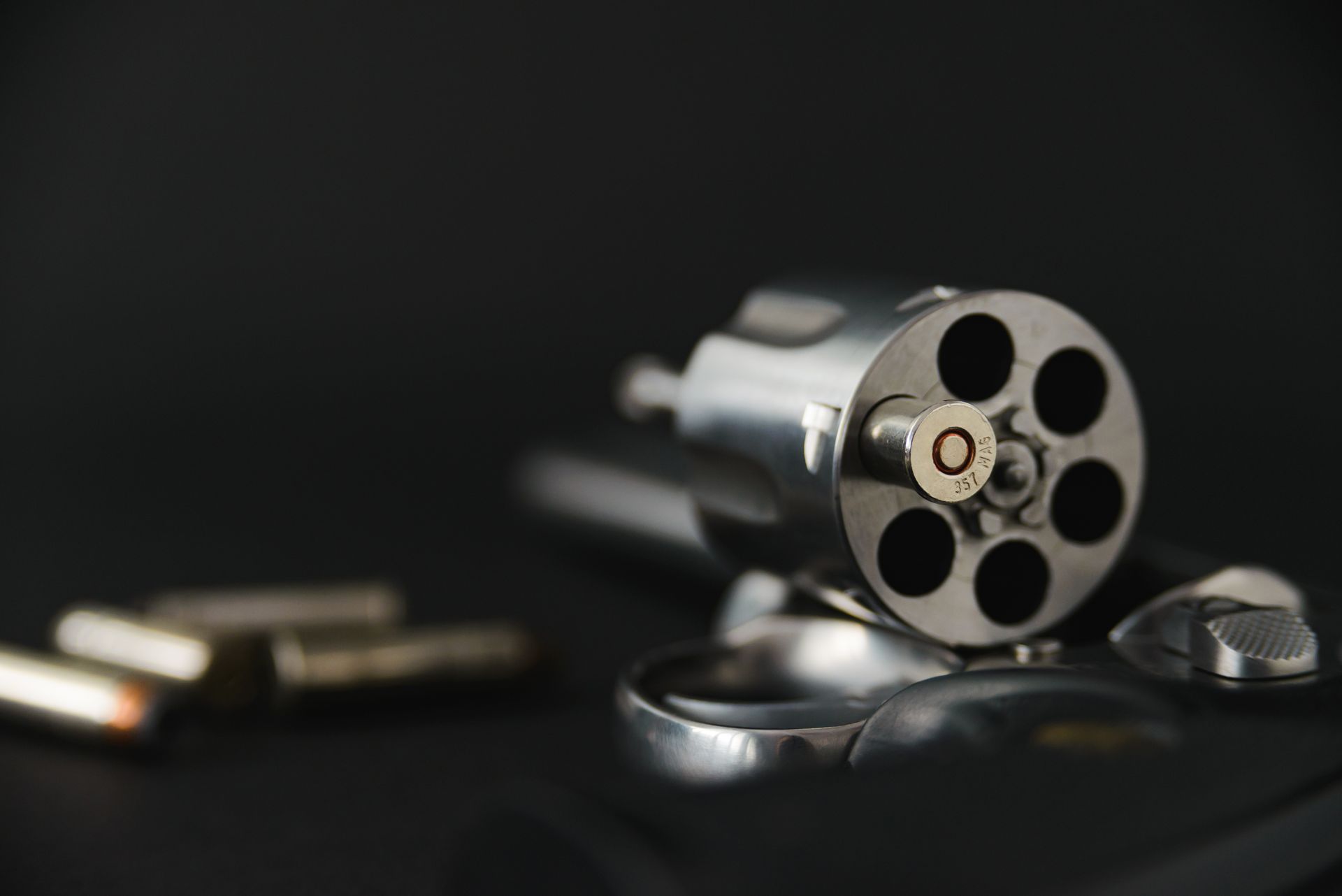 A revolver with one bullet in the chamber, on a black surface.