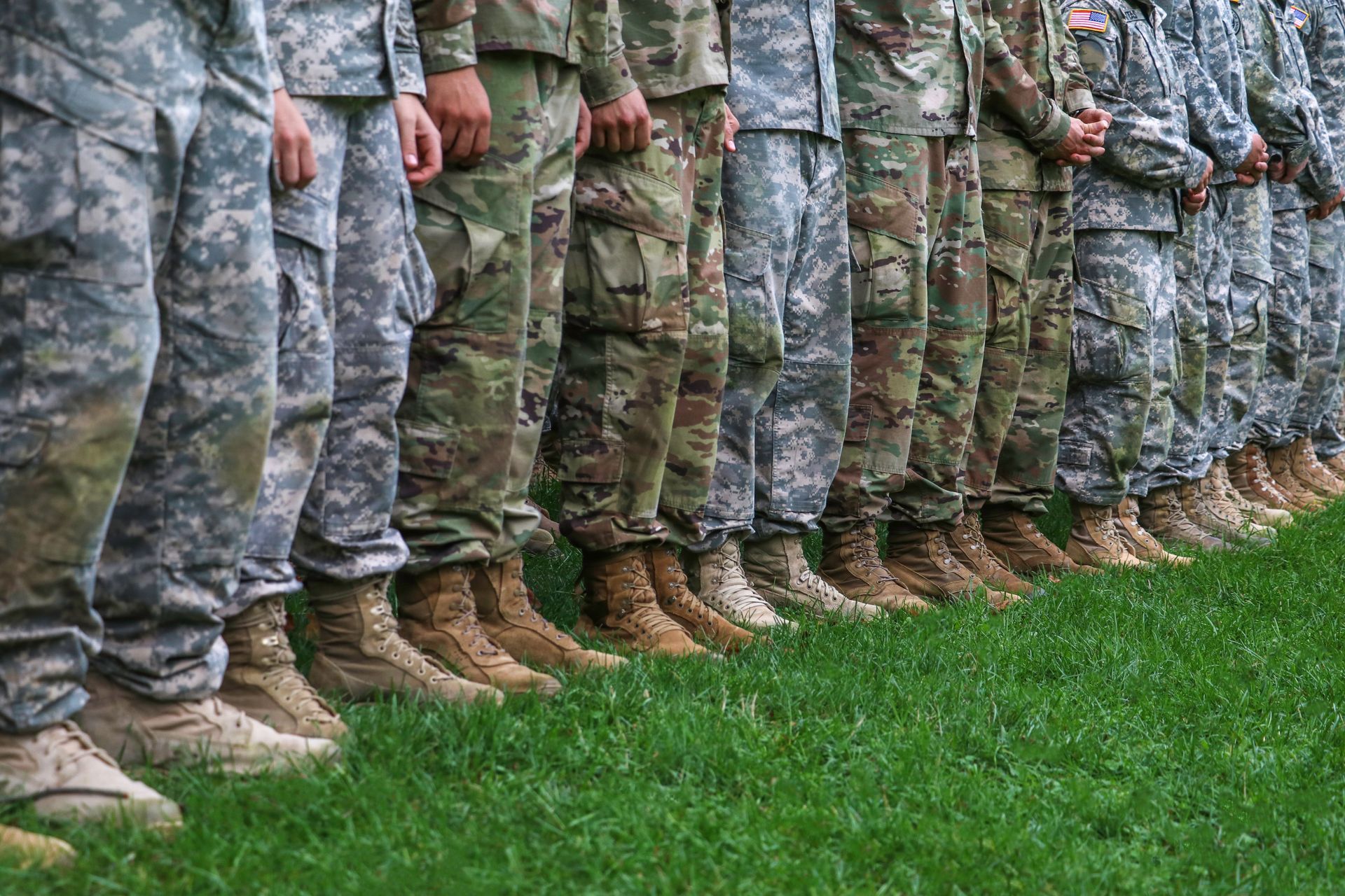 Military members standing in a row, wearing camouflage and tan boots.