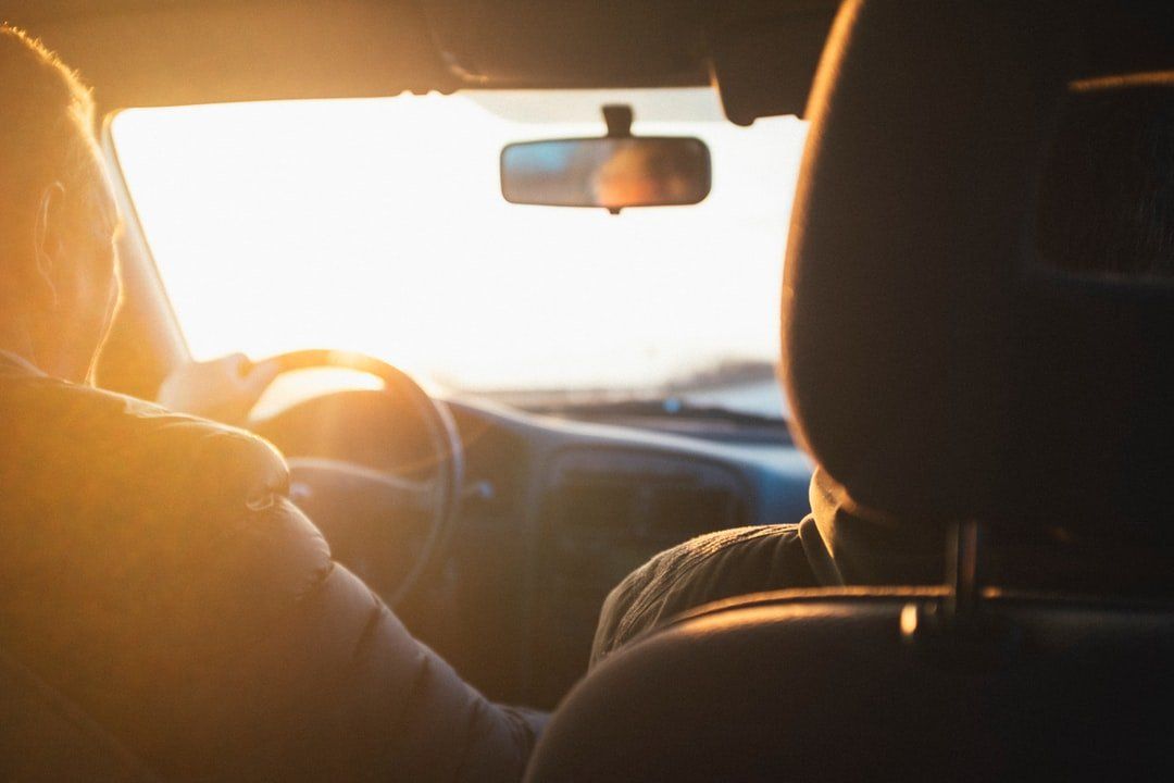 A man is driving a car with the sun shining through the windshield.