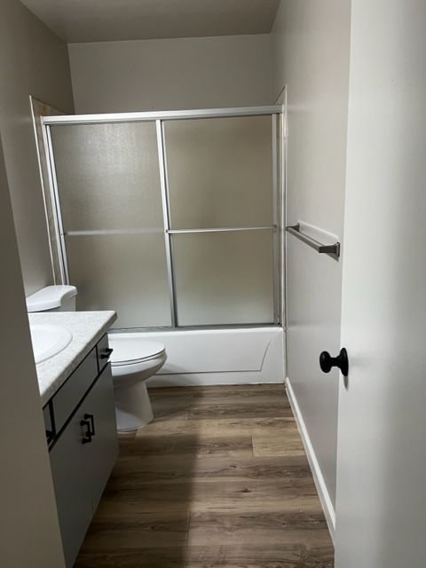 Bathroom with a shower, toilet, and vanity. Brown wood-look flooring and light walls.