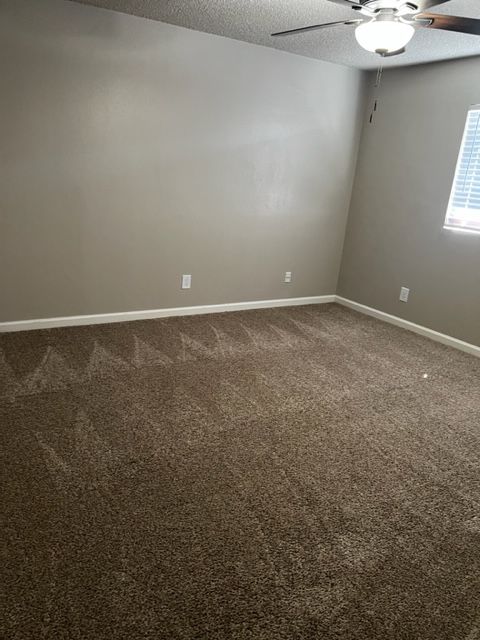 Empty bedroom with brown carpet, tan walls, and a window with blinds.