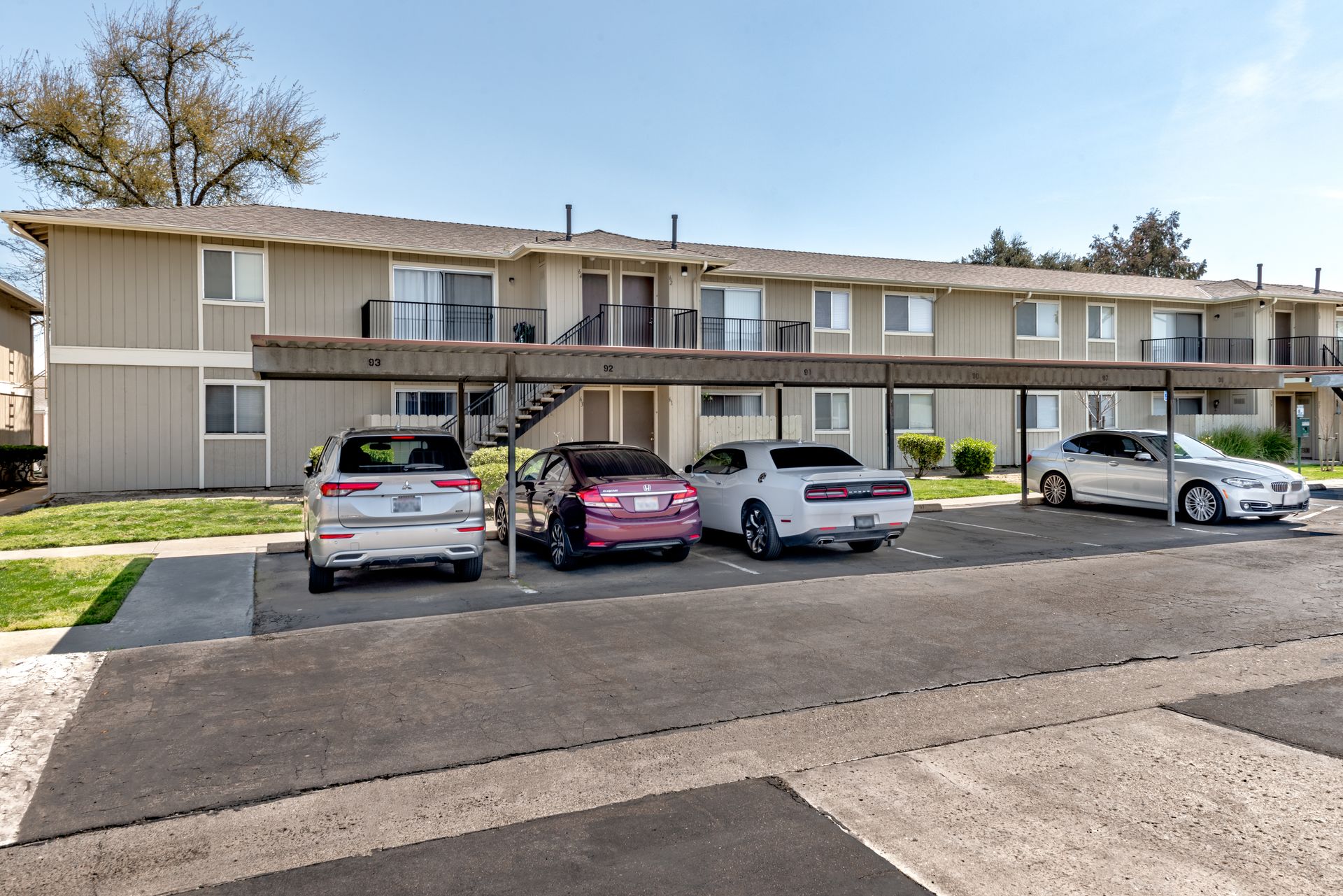 Apartment complex with covered parking; cars parked below; beige building, blue sky.
