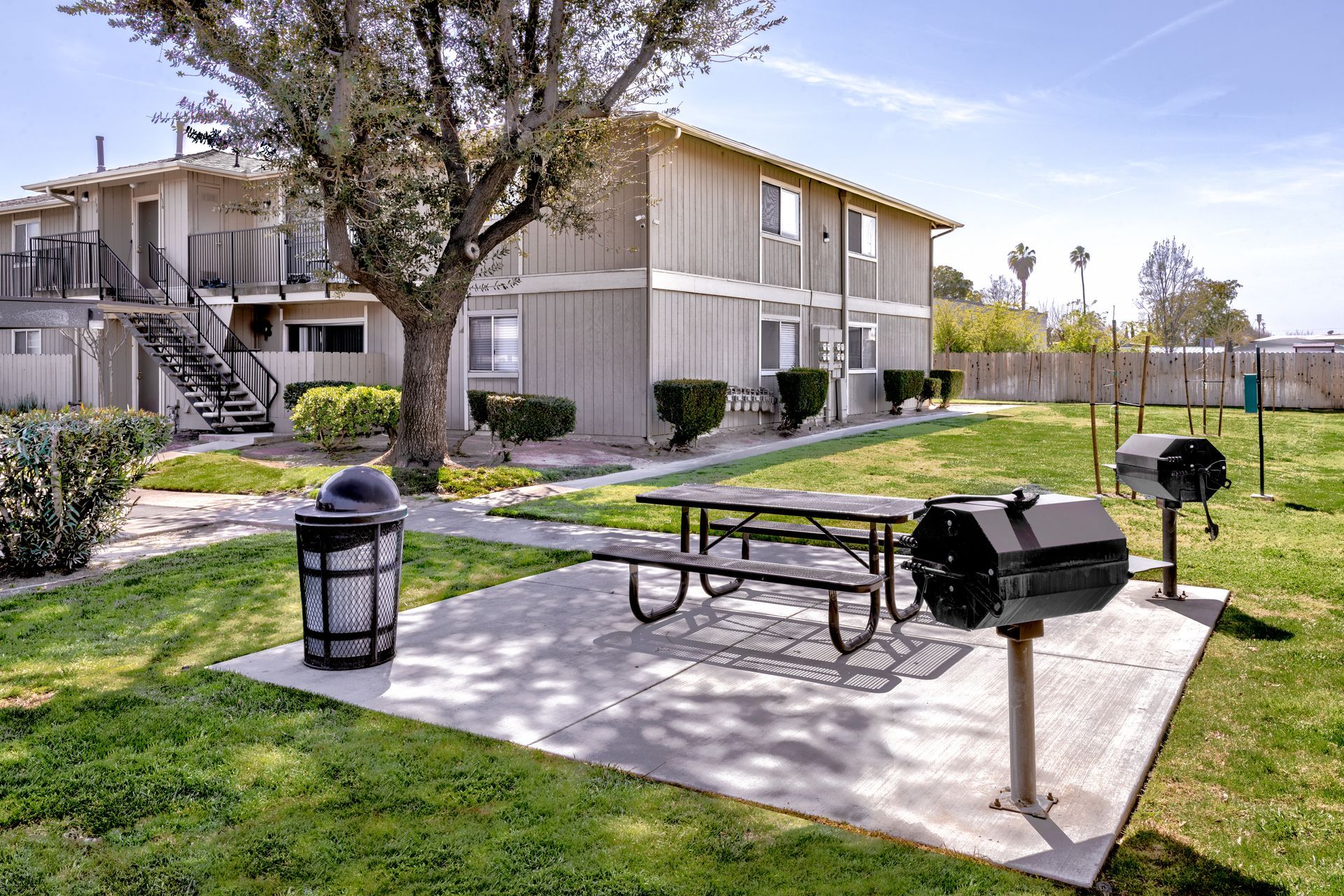 Apartment building with picnic table, grills, and trash can on a grassy lawn.