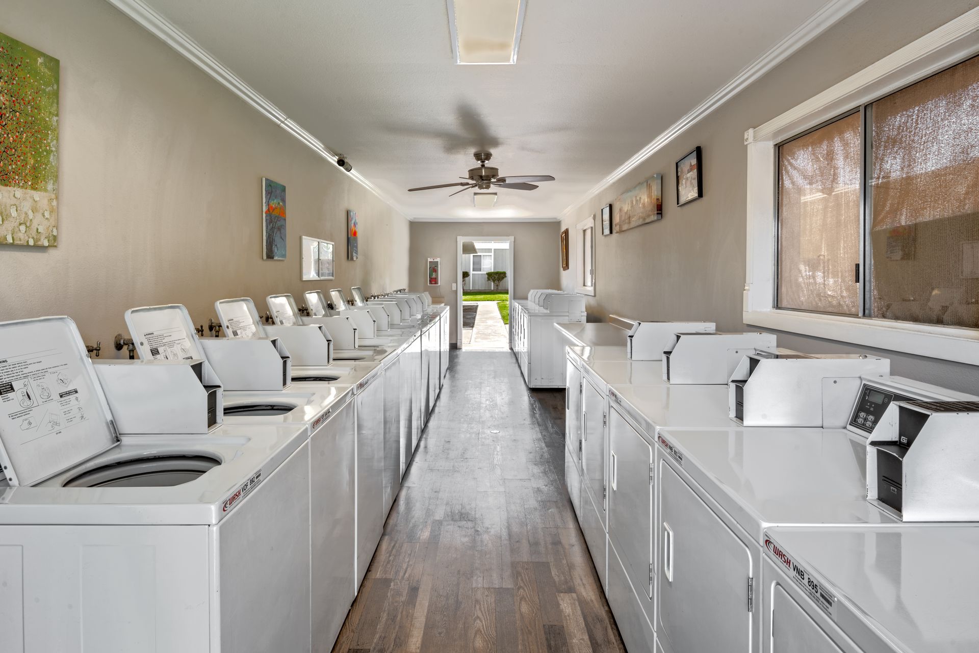 A long, well-lit laundromat with rows of white washing machines and dryers.