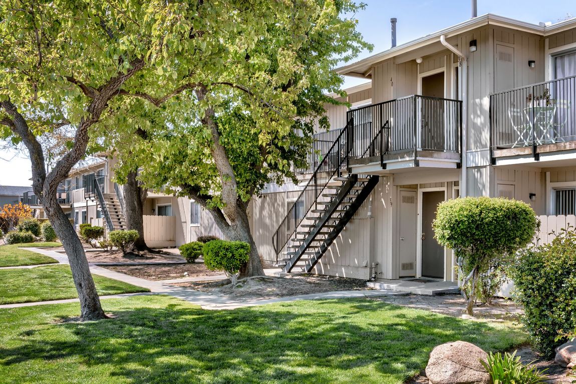 Apartment building with green lawn and trees, exterior with outdoor staircases, beige siding and railings.