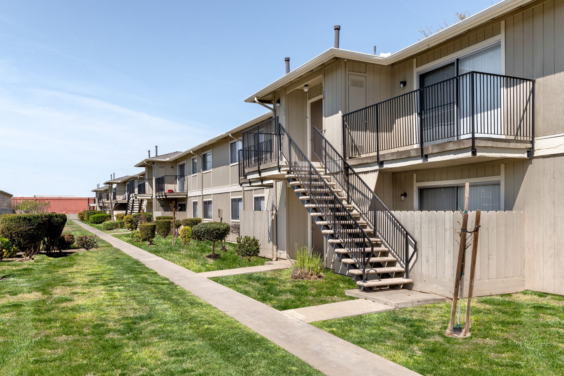 Apartment building with exterior staircases, beige siding, and green lawn on a sunny day.