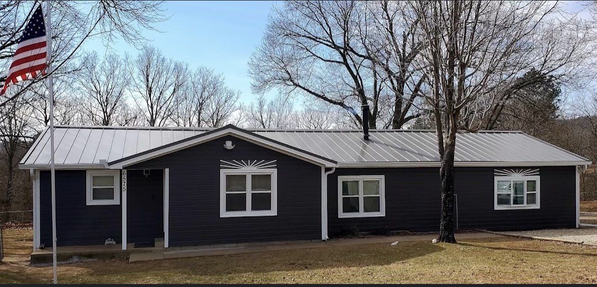 A black house with a white roof and an american flag flying in front of it.