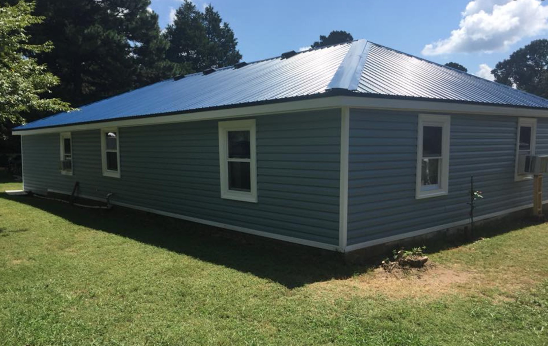 A blue house with a blue roof is sitting on top of a lush green field.