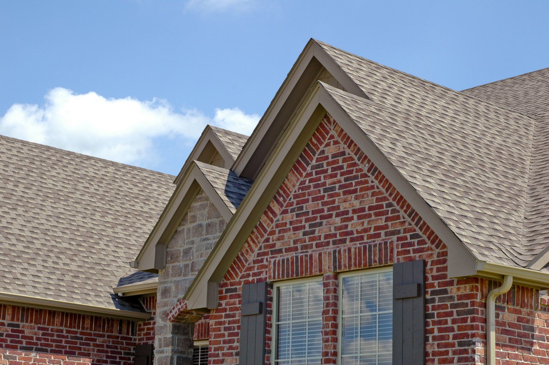 A brick house with a brown roof and a window with black shutters.