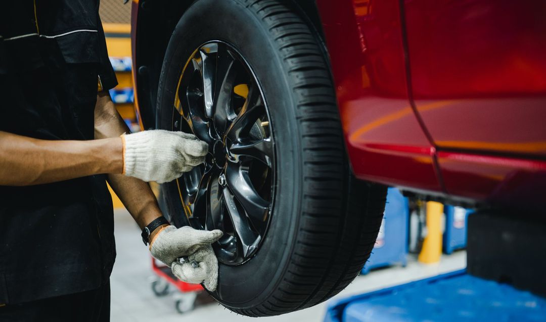 A man is changing a tire on a red car in a garage.